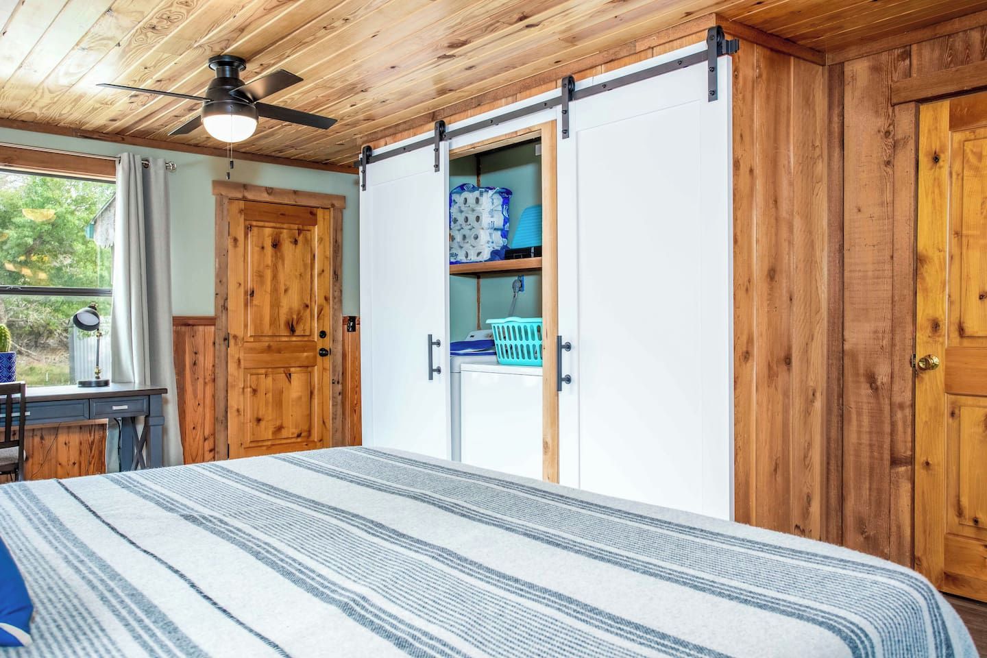 A bedroom with a bed, a desk, a ceiling fan, and a sliding door closet.