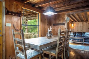 A wooden interior with a dining table, chairs, a sofa, and a hanging light fixture. - Old Fellows Farmhouse | 2BR with Country Views (Kerrville)