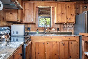 A kitchen with wooden cabinets, a stainless steel kettle, a microwave, and a refrigerator. - Old Fellows Farmhouse | 2BR with Country Views (Kerrville)
