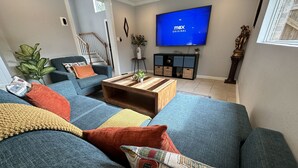 A living room with a large blue sofa, a wooden coffee table, and a television mounted on the wall. - 3 KING BEDS - 3 QUEEN - 4 TWINS - 5 BED ROOMS (Houston)