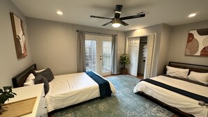 A bedroom with two beds, a ceiling fan, a large window with curtains, and a door leading to a closet. - 3 KING BEDS - 3 QUEEN - 4 TWINS - 5 BED ROOMS (Houston)