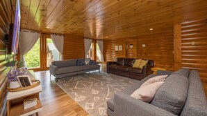 A cozy cabin interior with wooden walls and ceilings, a grey sofa, a brown leather couch, and a patterned rug.