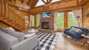 A log cabin interior with a fireplace, a sofa, a blue couch, and a staircase.