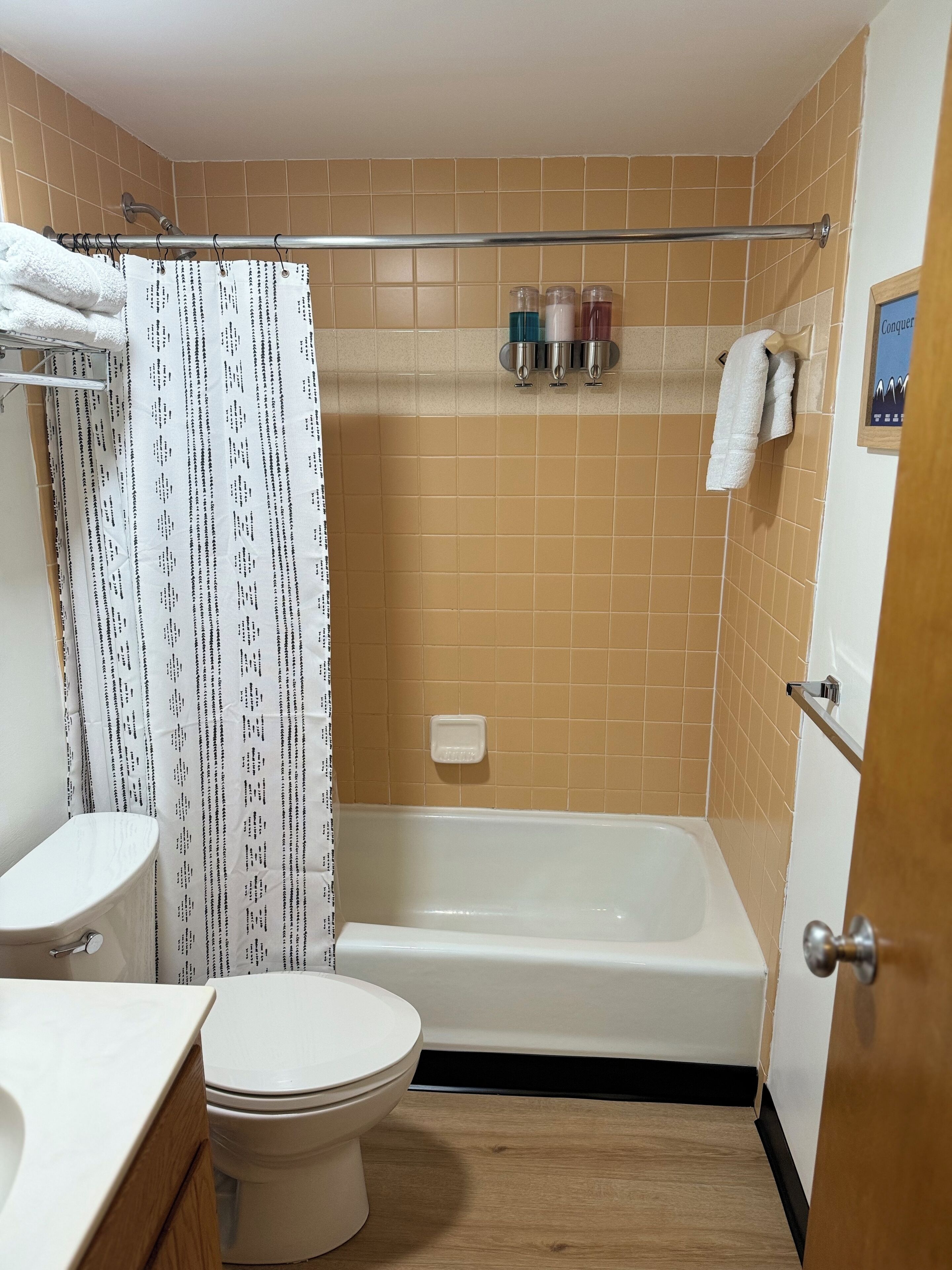 Een badkamer met toilet, wastafel en bad. Een douchegordijn met dessin, een handdoekhouder en een zeepbakje.
