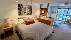 A modern bedroom with a large bed, a nightstand, a bedside table, a dresser, a window with a view, and a ceiling fan. - Smooth 2-minute ski to Lift Ski-in Ski-out • Smuggs Condo ⭐️  (Jeffersonville)