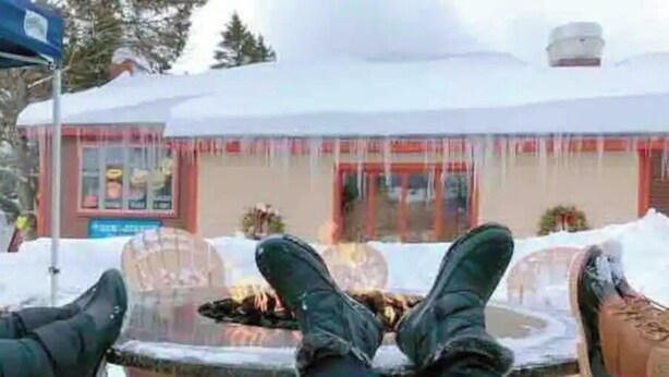 A person sitting by a glass table with a fire, legs crossed, in a snowy outdoor setting. - Smooth 2-minute ski to Lift Ski-in Ski-out • Smuggs Condo ⭐️  (Jeffersonville)