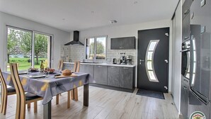 A modern kitchen with a dining area, large windows, and a view of the outdoors. - Le Clos des Pommiers (PAIMPOL)