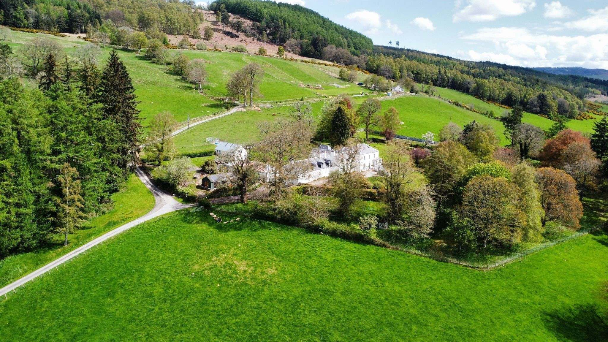 Eine ländliche Landschaft mit einem weißen Gebäude, umgeben von grünen Feldern und Bäumen.