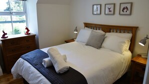 A neatly made bed with a blue blanket and a rolled towel, wooden headboard, bedside lamps, and a dresser with drawers. - The Gardeners Cottage -  Retreat Group (Pitlochry)