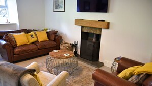 A cozy living room with a brown leather sofa, a round coffee table, and a fireplace. - The Gardeners Cottage -  Retreat Group (Pitlochry)