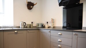 A kitchen with grey cabinets, a kettle, a toaster, and a decorative wall hanging. - The Gardeners Cottage -  Retreat Group (Pitlochry)