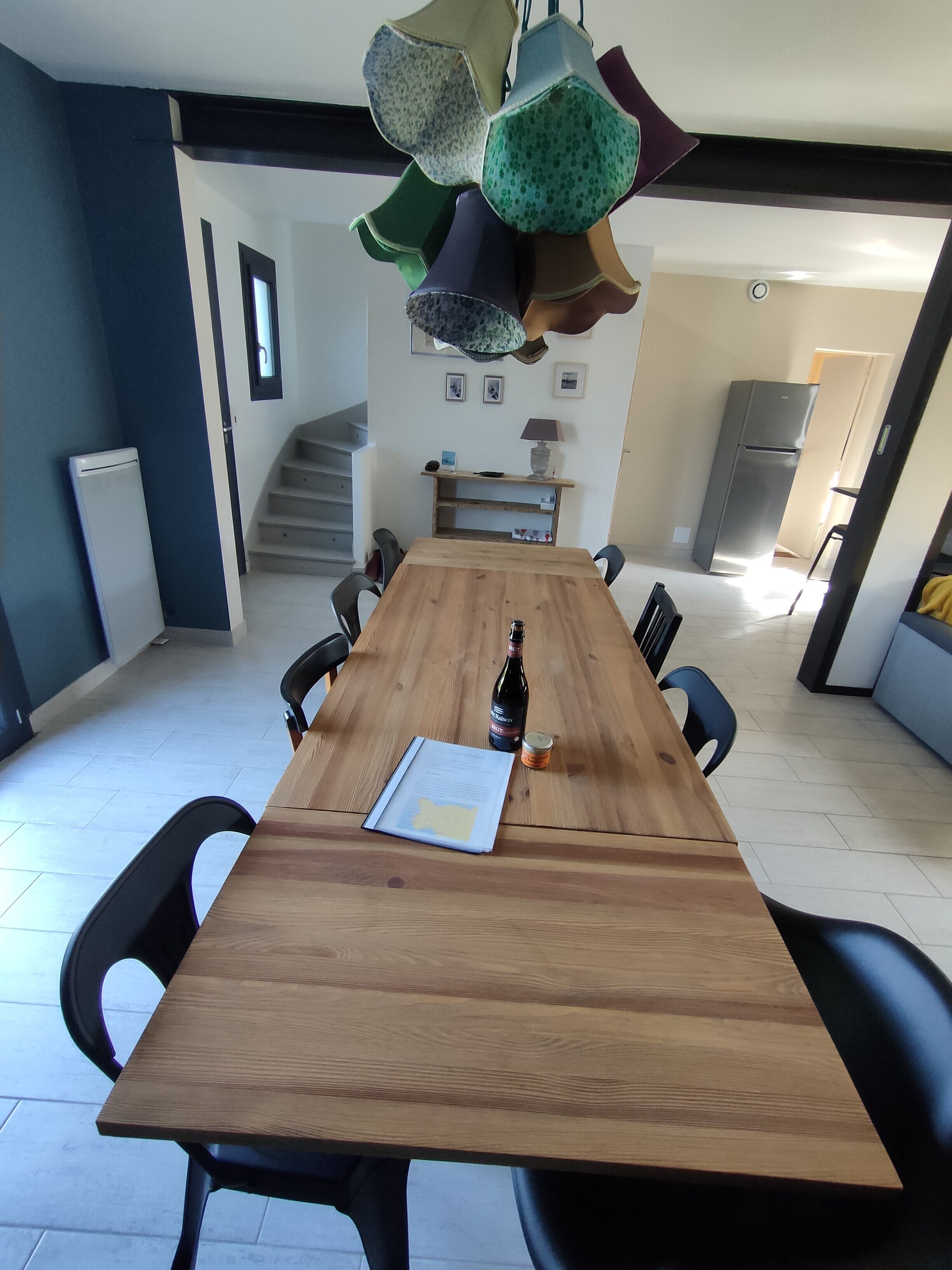Un espace repas avec une table en bois, des chaises, une bouteille et un menu.