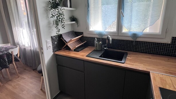 Eine kleine Küche mit einer Holz Arbeitsplatte, einer eingebauten Spüle und einem Fenster mit Vorhängen.