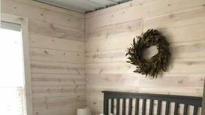 Een slaapkamer met een houten wand, een bed met witte beddengoed, een nachtkastje met een lamp en een krans aan de muur.