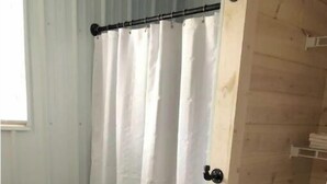 Een badkamer met douchegordijn, toiletrolhouder, wastafel en houten vloer.