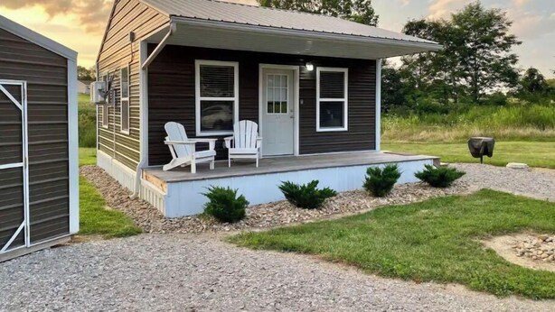 Een klein, gelijkvloers huis met een veranda, twee witte stoelen en een grindpad.