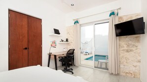 A bedroom with a bed, a desk, a chair, a TV, and a view of a pool.