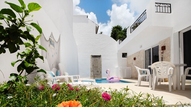 A white building with a pool, white outdoor furniture, and colorful flowers in the foreground.