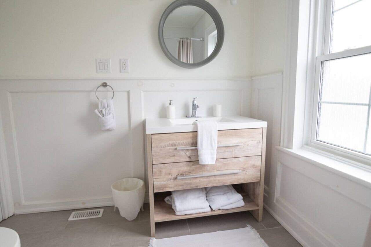 A bathroom with a white vanity, a round mirror, and a window.