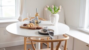 Een ronde witte tafel met een fles wijn, glazen, brood en een vaas met bloemen.