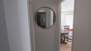 A hallway with a geometric-patterned bench, a round mirror on the wall, and a view into a dining area with a table and chairs. - Attached Unit, a few minute walk from the Beach (Santa Barbara)