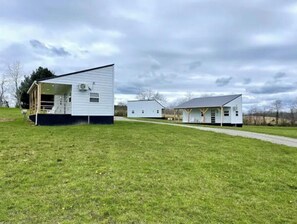 A modern, single-story building with a covered porch and a small attached structure. - Makenna-NEW tiny home with shared fishing pond (Athens)