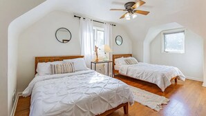 Un dormitorio con dos camas, un ventilador de techo, una ventana y un espejo en la pared.
