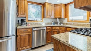 Una cocina con armarios de madera, electrodomésticos de acero inoxidable, encimeras de granito y una ventana con persianas.