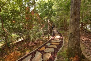 Meander through a serene forested area along a natural stone path, surrounded by lush trees and shrubs.