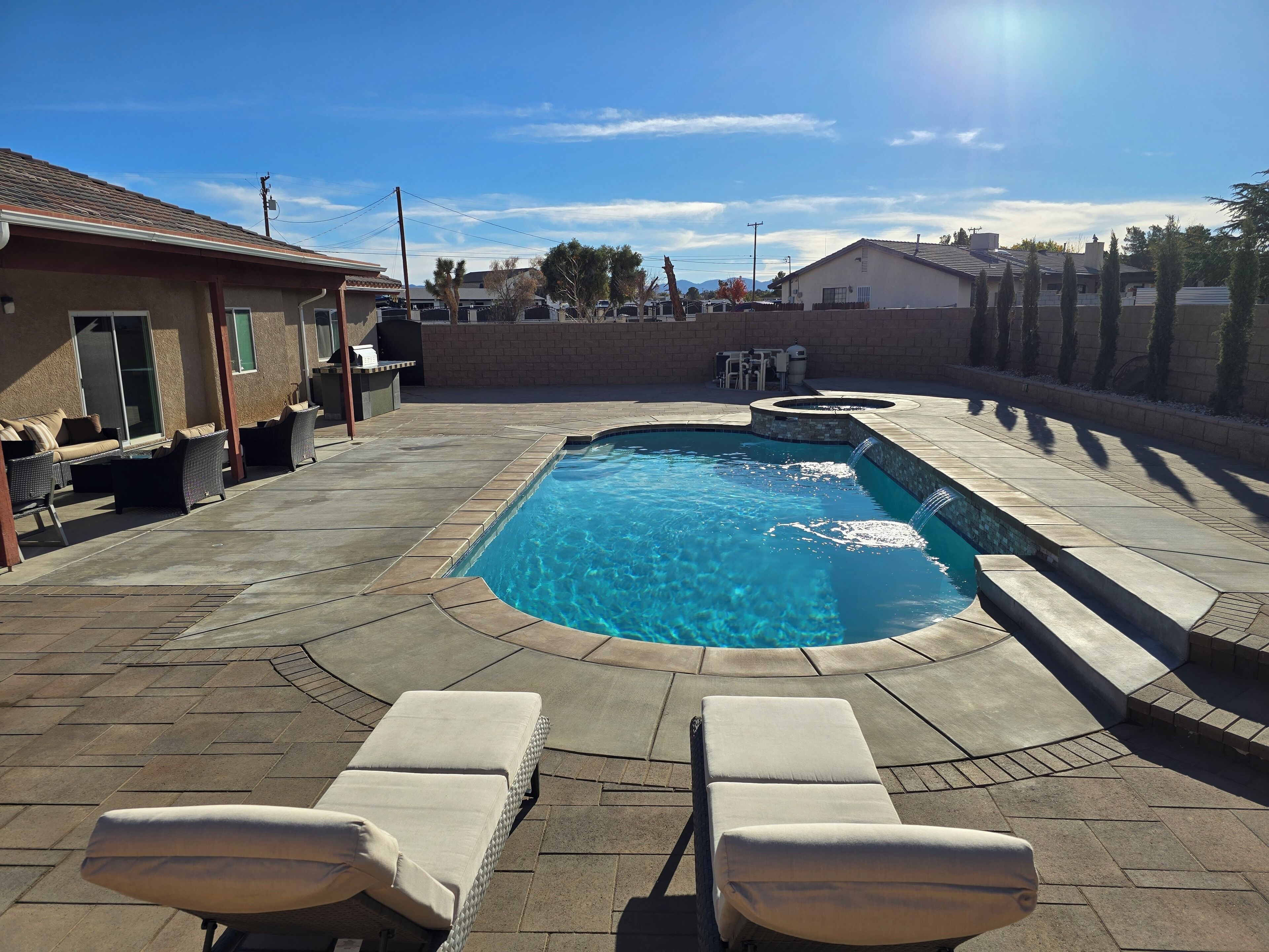 A rectangular swimming pool with a small waterfall feature, surrounded by lounge chairs and a patio area.