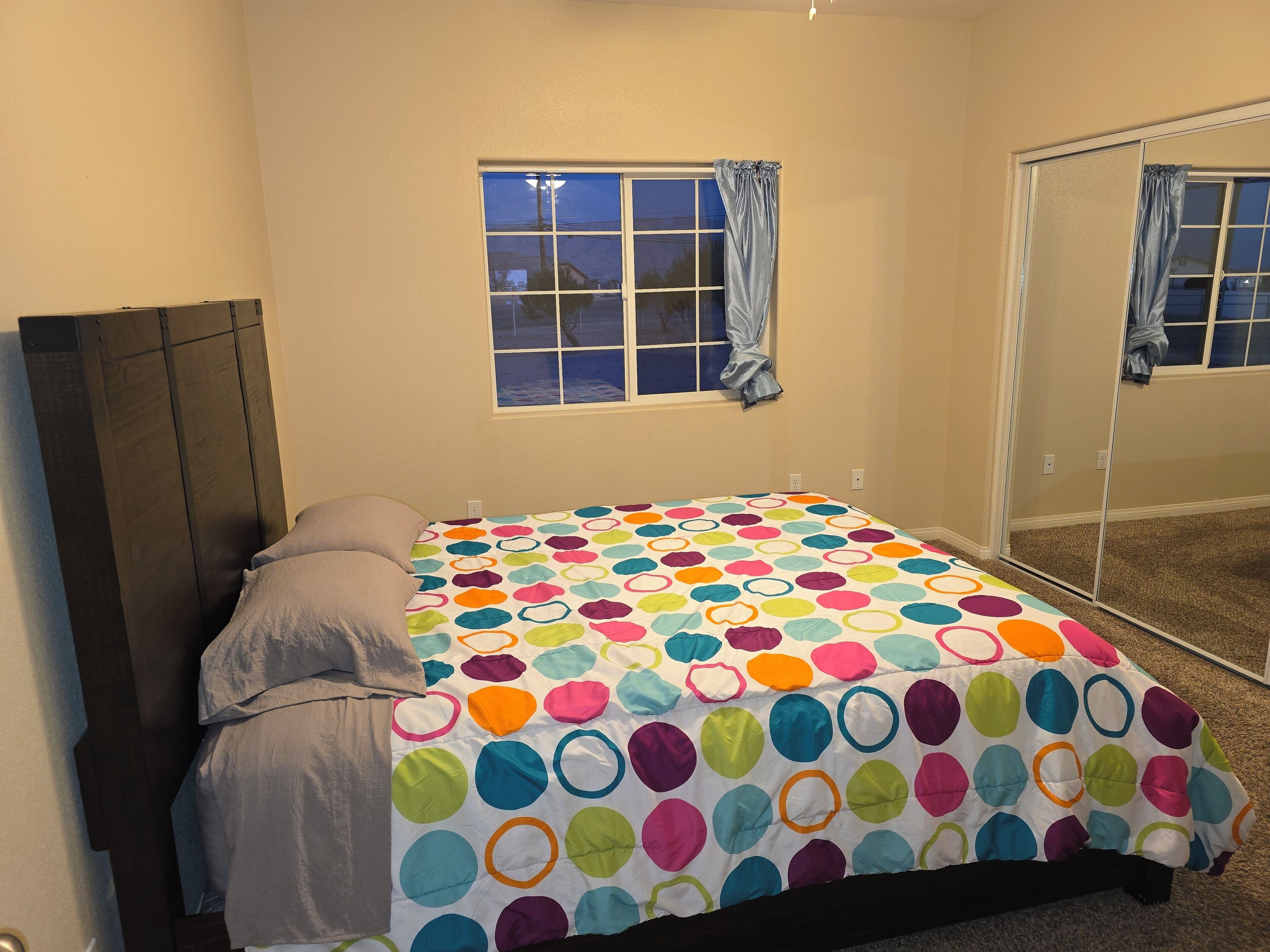 Un dormitorio con cama, ventana con cortinas y un espejo.