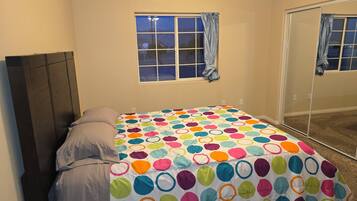 Un dormitorio con cama, ventana con cortinas y un espejo.