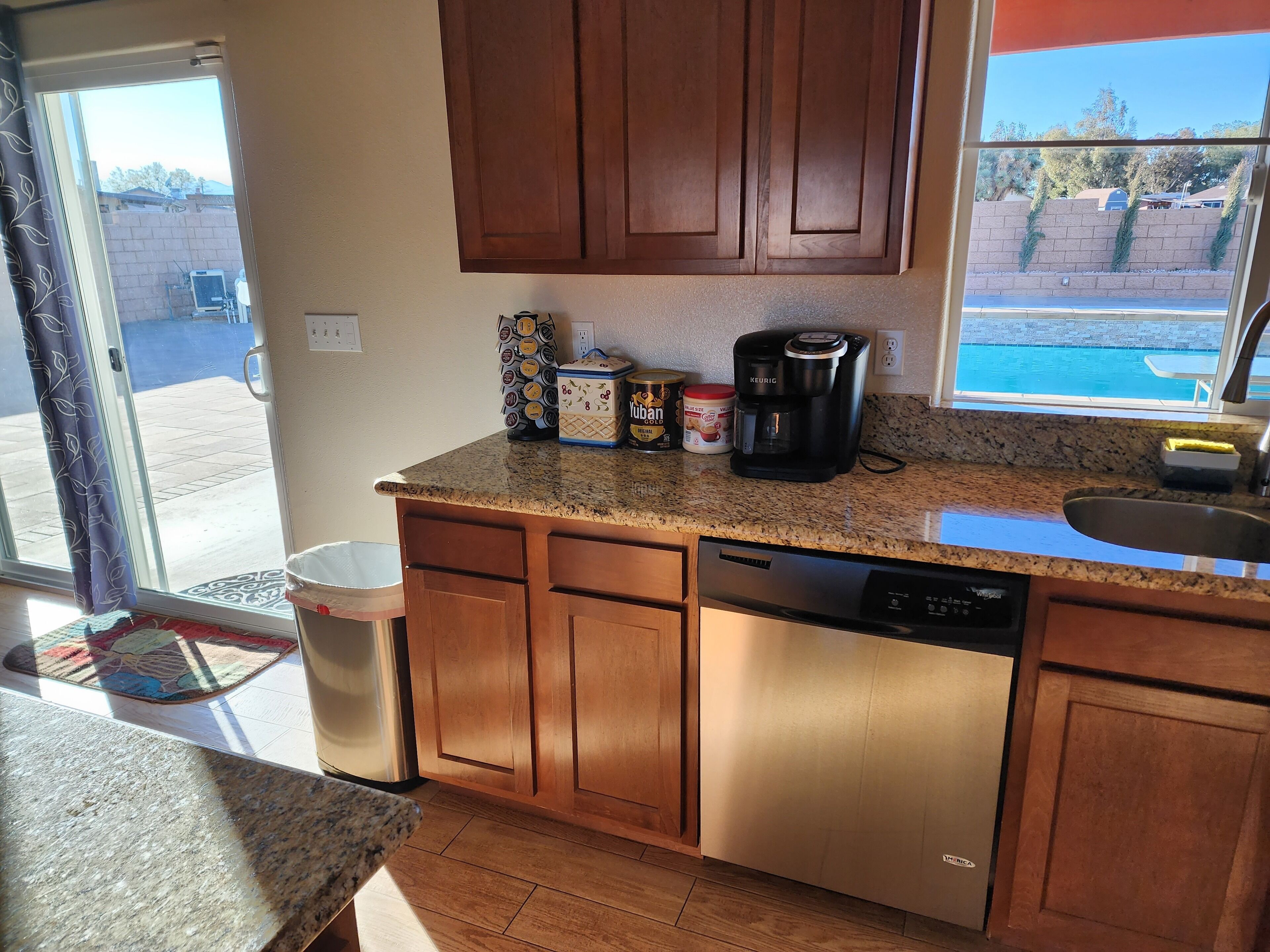 A kitchen with wooden cabinets, a granite countertop, a coffee maker, and a view of a swimming pool.