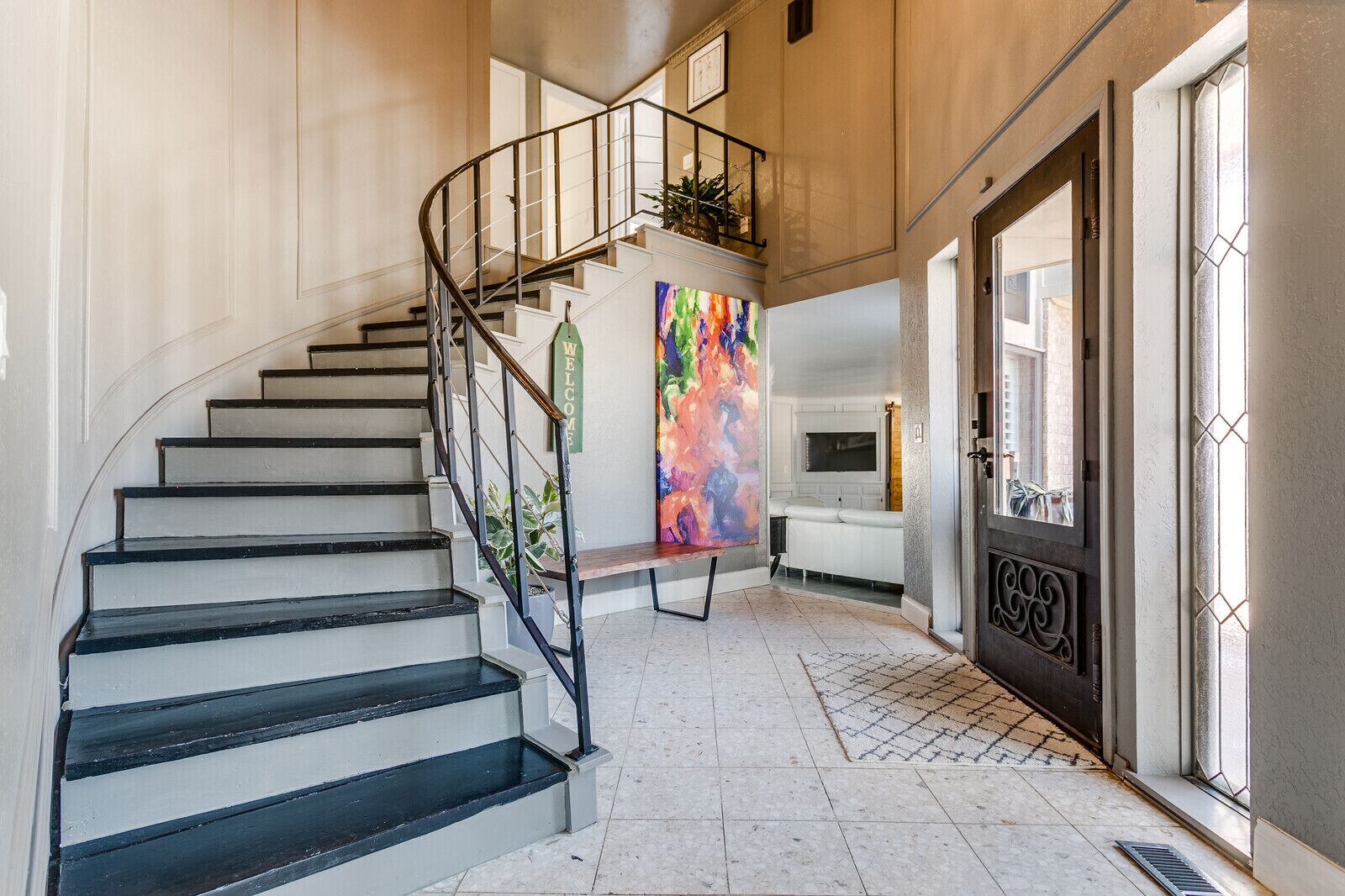 Escadaria com corrimão de metal que leva a um patamar com uma pintura abstrata colorida.