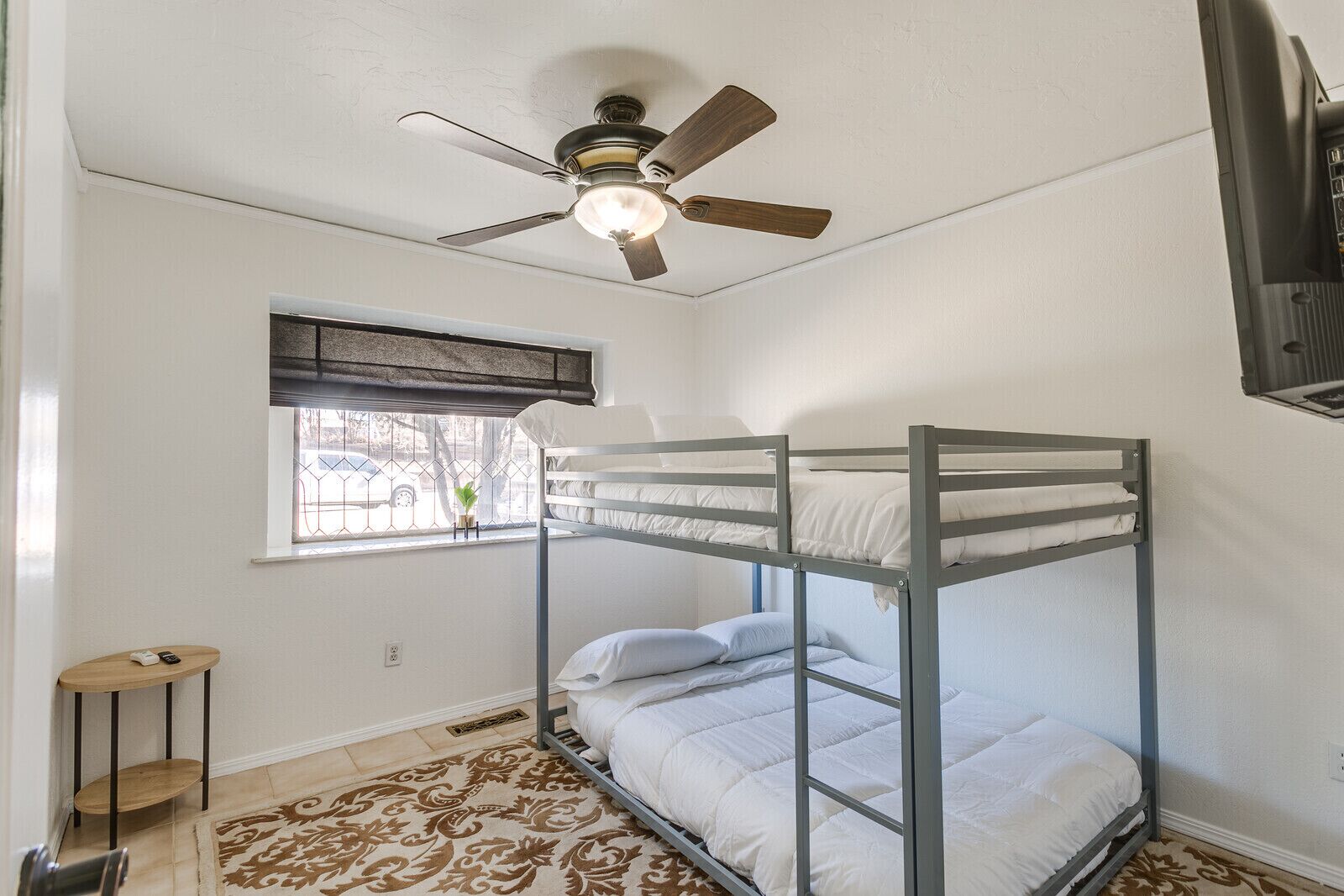 Habitación con literas, ventilador de techo, ventana con vistas y alfombra estampada.