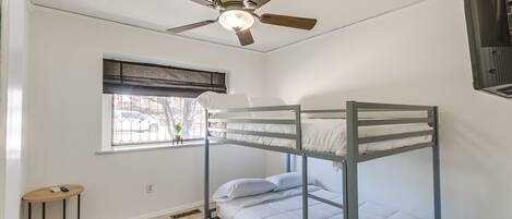 Habitación con literas, ventilador de techo, ventana con vistas y alfombra estampada.