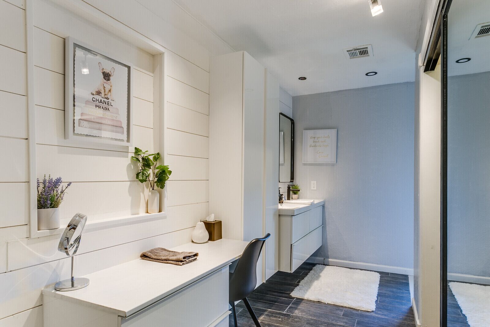 A modern bathroom with a white vanity, a mirror, a potted plant, and a framed picture of a dog.