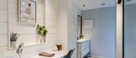 A modern bathroom with a white vanity, a mirror, a potted plant, and a framed picture of a dog.