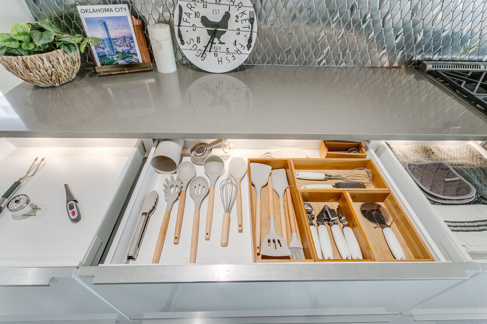 A kitchen drawer with various utensils and a decorative clock.