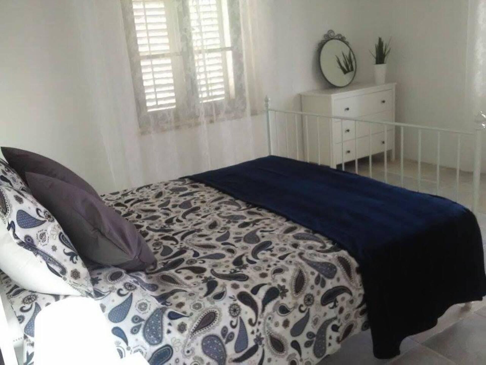 A bedroom with a bed, a dresser, a mirror, and a window with blinds.