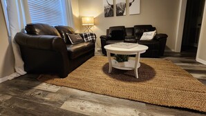 Een woonkamer met een bruine leren bank, een witte salontafel en een bruin vloerkleed. Op de muur hangen drie zwart-wit ingelijste foto's.