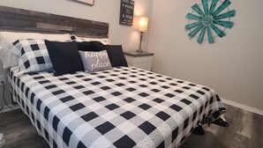 Een slaapkamer met een geruite sprei, een nachtkastje met een lamp, en decoratie aan de muur, waaronder een bord en een decoratief wandobject.