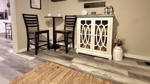 Een woonkamer met een aan de muur bevestigde televisie, een kast met decoratieve objecten en twee stoelen.