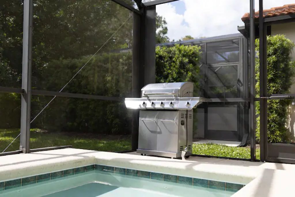 A backyard with a swimming pool, a grill, and a screened area.