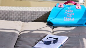 A balcony with a view of a harbor, a blue bag with text, and a pair of sunglasses on a cushion.