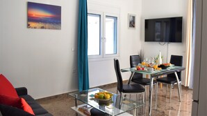 A modern living room with a glass dining table, black chairs, a red couch, a TV mounted on the wall, and a window with blue curtains.