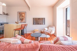 Una sala de estar acogedora con sofá, una pequeña mesa de comedor, una silla y una zona de cocina con microondas y hervidor.