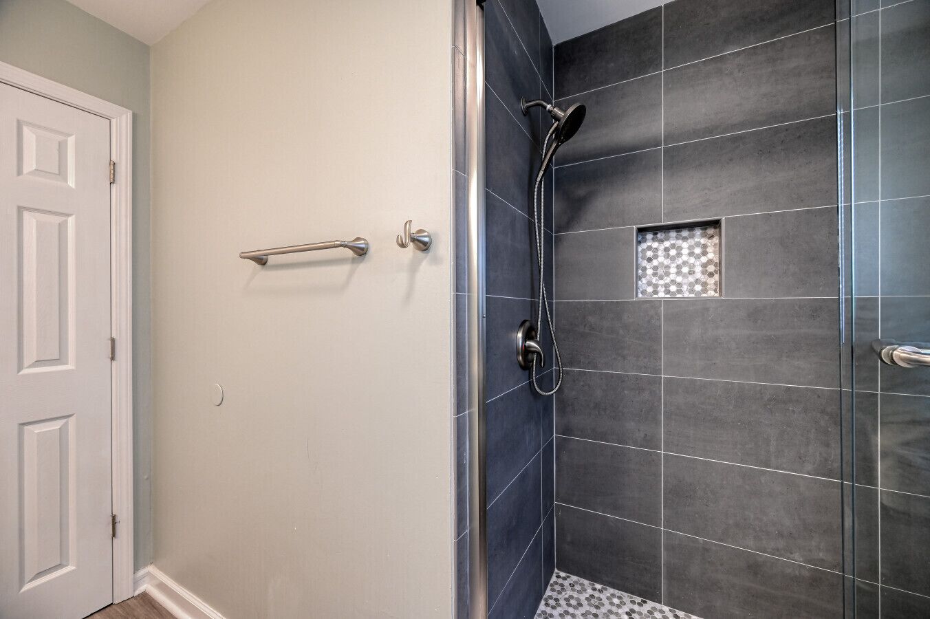 A shower with dark tiles and a small decorative tile pattern on the wall.