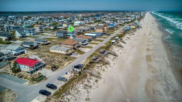 An aerial view of a coastal residential area with houses, a beach, and a road.