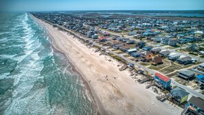 An aerial view of a coastal residential area with houses along the beach, a clear sky, and a calm sea.